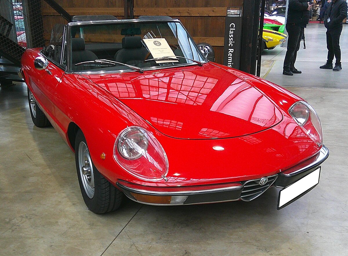 Alfa Romeo 2000 Spider Veloce aus dem Jahr 1974. Im Jahr 1969 begann für den Alfa Romeo Spider die Fastback-Ära. Diese so genannte  coda-tronca-Optik  gab dem Zweisitzer einen modernen Touch. Auch im Innenraum gab es Änderungen. Auffälligstes Merkmal waren die zwei  Eisbecher , die jetzt die Instrumente einrahmten, was ungemein sportlich aussah. Die Scheinwerferverglasungen waren in einigen Ländern im Lieferumfang enthalten. Angetrieben wird der Spider von einem Vierzylinderreihenmotor mit einem Hubraum von 1962 cm³ und einer Leistung von 131 PS. Classic Remise Düsseldorf am 11.01.2025.