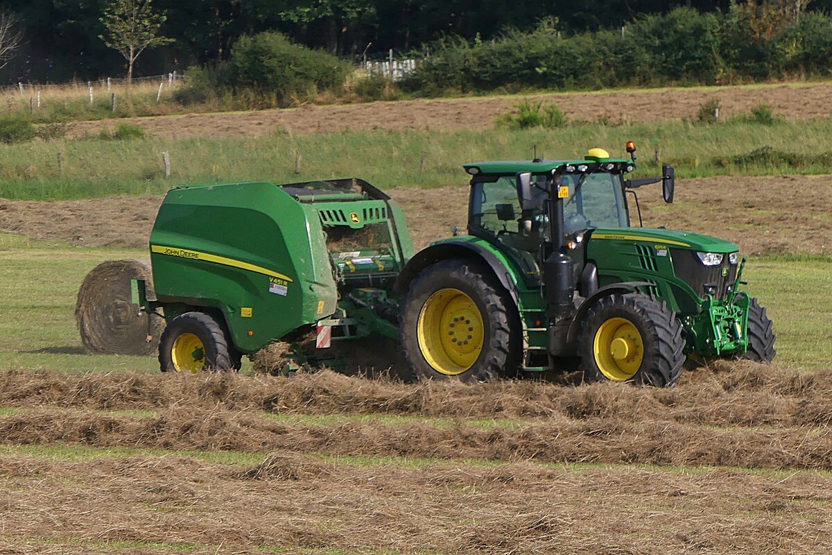 Heuernte: John Deere Traktor mit John Deere Rundballenpresse beim  Aufsammeln  und Pressen des Heues. 08.2024