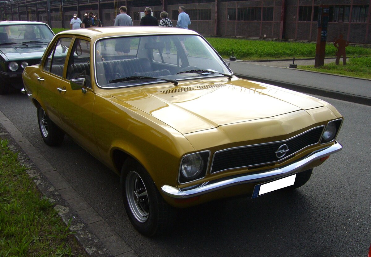 Opel Ascona A als viertürige Limousine, gebaut von 1970 bis 1975. Das völlig neue Modell sollte die Lücke zwischen dem Einsteigermodell Kadett und dem Mittelklassemodell Rekord füllen. Der Wagen stand ab November 1970 bei den Händlern. Hier wurde ein Ascona im Farbton DD Gold abgelichtet, wie er ab September 1973 produziert wurde. Dieses ist am schwarzen Kunststoffkühlergrill zu erkennen. Der Erstbesitzer hat als Motorisierung für diesen Wagen die Motorversion 1.6 gewählt. Der Vierzylinderreihenmotor hat einen Hubraum von 1584 cm³ und leistet 68 PS. Ein solch viertüriger Ascona A war ab DM 10.345,00 zu haben. Oldtimer-Revival auf dem Gelände der Kokerei Zollverein in Essen am 28.07.2024.