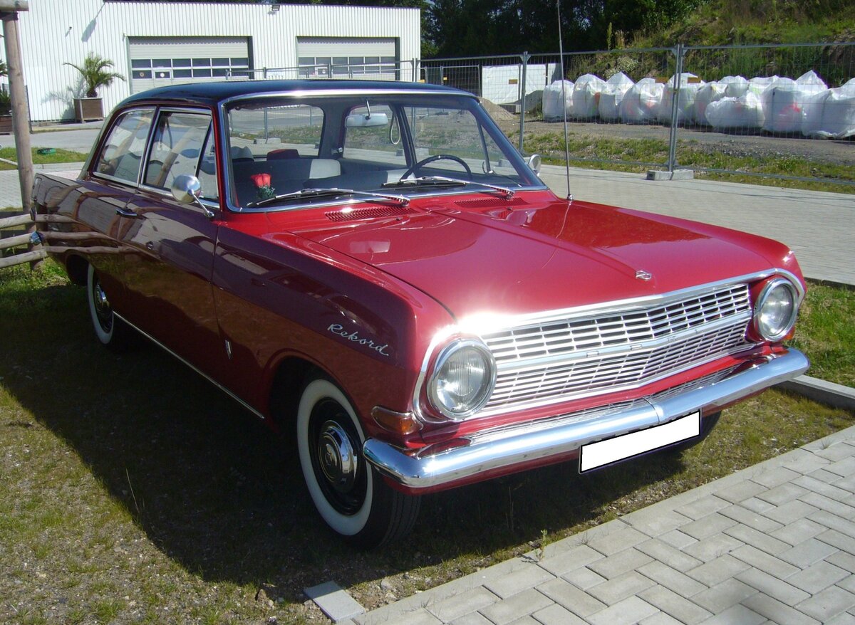 Opel Rekord A in der Karosserieversion zweitürige Limousine. Produziert wurde das Modell von 1963 bis 1965. Bei diesem Modell konnte man die Verwandtschaft zum GM-Konzern klar erkennen. Die Karosserie hat Ähnlichkeit mit einem  geschrumpften  Chevy II. Für dieses Modell waren etliche Motorisierungen lieferbar: 1.5l mit 55 PS, 1.7l mit 60 PS oder 67 PS und sogar ein Sechszylinderreihenmotor mit 2605 cm³ Hubraum und 100 PS. Der abgelichtete Rekord A wurde 1963 erstmalig zugelassen und ist in der Farbkombination monzarot/schwarz lackiert. Als Rekord 1500 war eine solch zweitürige Limousine ab DM 6.830,00 erhältlich. Beim ersten Zwischenstopp der Ausfahrt des Panoramatreffen der Alt-Opel IG am Luftschiffhangar des Flughafen Essen/Mülheim am 10.08.2024. 