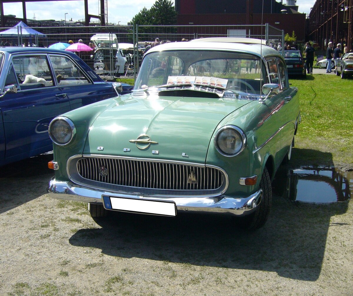 Opel Rekord P1 in der Karosserieversion zweitürige Limousine, gebaut von 1957 bis 1960. Während seiner 35-monatigen Produktionszeit, baute Opel 384.692 Limousinen (zwei- und viertürig), 109.282 Kombimodell CarAvan und 15.136 Kastenlieferwagen (ohne hintere seitliche Verglasung) von diesem Modell. Motorisiert war der P1 mit einem Vierzylinderreihenmotor mit einer Leistung von 45 PS aus einem Hubraum von 1488 cm³. Gegen einen Aufpreis von DM 75,00, konnte man einen 1.7l Motor mit 55 PS ordern. Da der P1 auch in die USA exportiert wurde und dort über das Buick-Händlernetz vertrieben wurde, erhielt er häufig den Spitznamen  Bauern-Buick . Der gezeigte P1 im Farbton graugrün wurde 1958 erstmalig vermutlich in der Schweiz zugelassen. Darauf lassen die Badges am Kühlergrill schließen. Einmal das Logo des GM-Zweigwerkes im schweizerischen Biel (erkennbar an den drei Bergspitzen) und dem Schild des TCS (T ouring C lub S uisse). Oldtimer-Revival auf dem Gelände der Kokerei Zollverein in Essen am 28.07.2024.