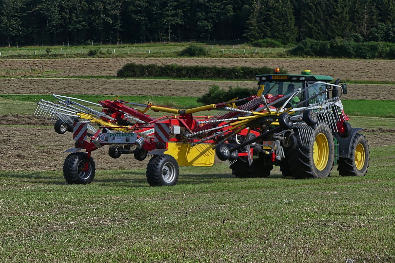 Heuernte: Pottinger Heuwender, gezogen von einem John Deere Traktor, aufgenommen bei der Auffahrt auf das Feld um das trockene Heu zu Schwaden. Feld. 08.2024