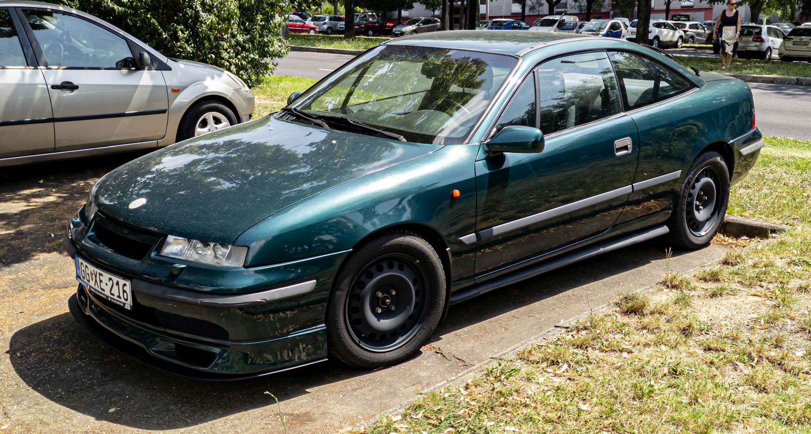 Hier ist ein dunkelrüner Opel Calibra mit dem 2 Liter 16 Ventil Motor zu sehen. Der Besitzer hat dementsprechend ein Kennzeichen ausgewählt. Die Aufnahme stammt von Juli, 2024.