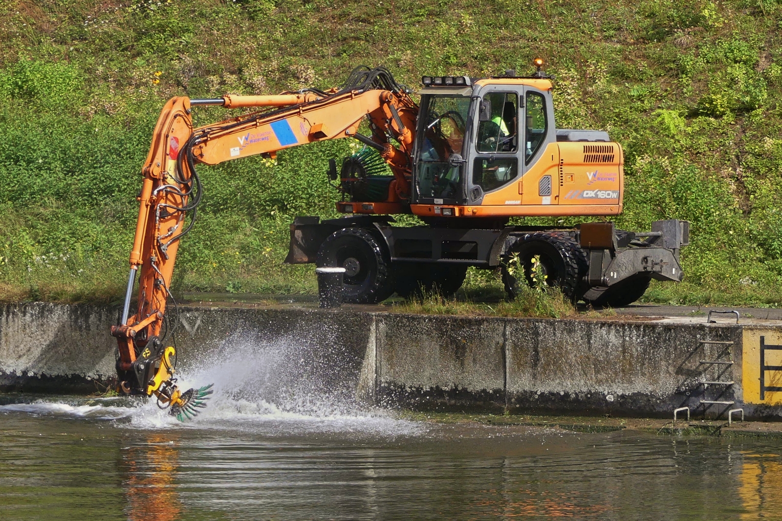 Hydraulikbagger Doosan DX 160 W, aufgenommen beim Reinigen der Kaimauer an einem Kanal. 09.2024