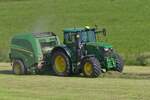 John Deere 6215 R, mit John Deere V 451 R Rundballenpresse, auf einem Feld.