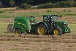 Heuernte: John Deere Traktor mit John Deere Rundballenpresse beim  Aufsammeln  und Pressen des Heues.