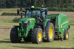 Heuerente: John Deere Traktor kommt mit der Rundballenpresse auf dem Feld an.